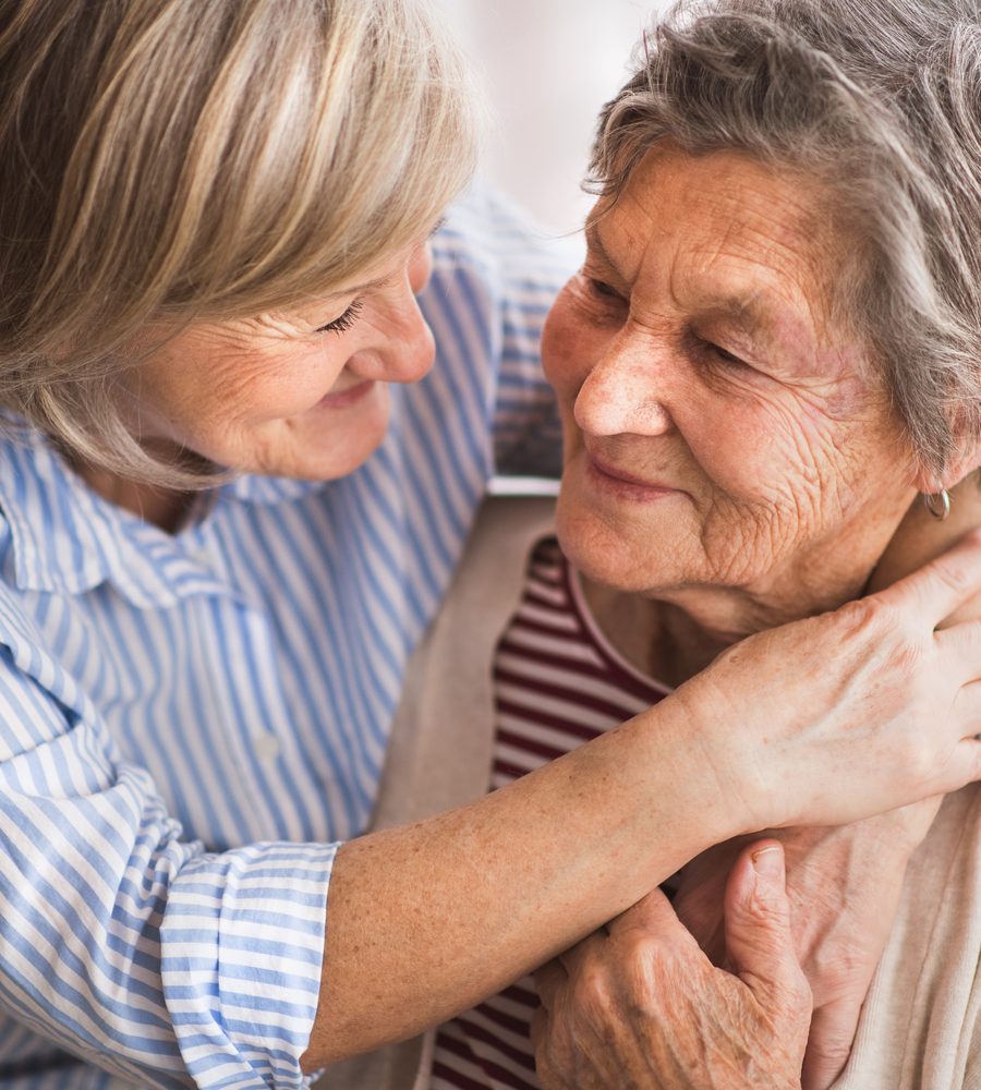 Betreuerin umarmt eine Seniorin zu Hause